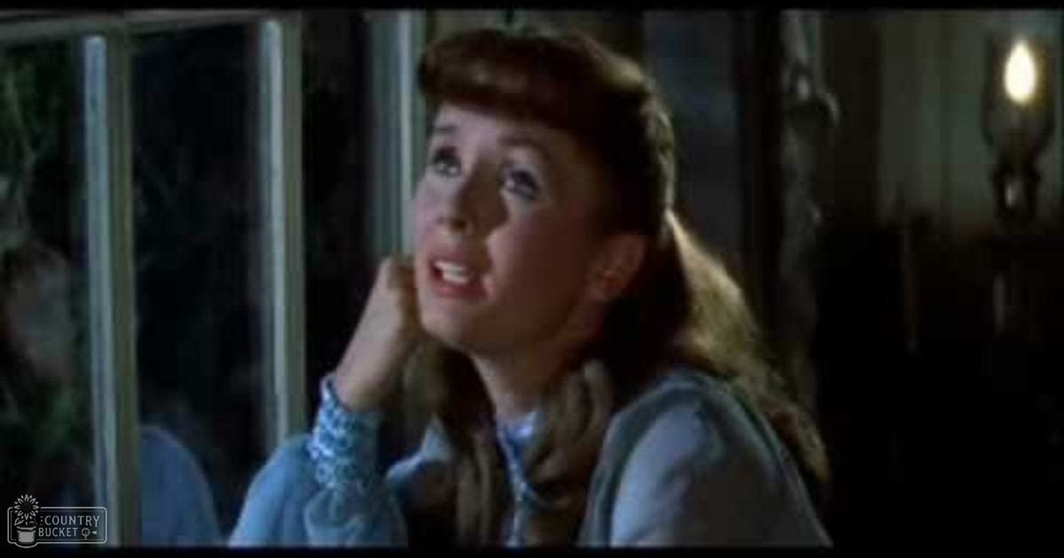 Young adult female wearing a light blue and white patterned shirt indoors near evening lighting.