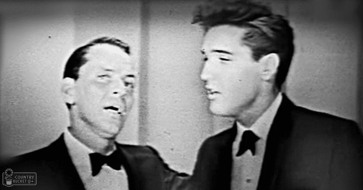 Two middle-aged men in formal attire stand indoors against a plain dark background.