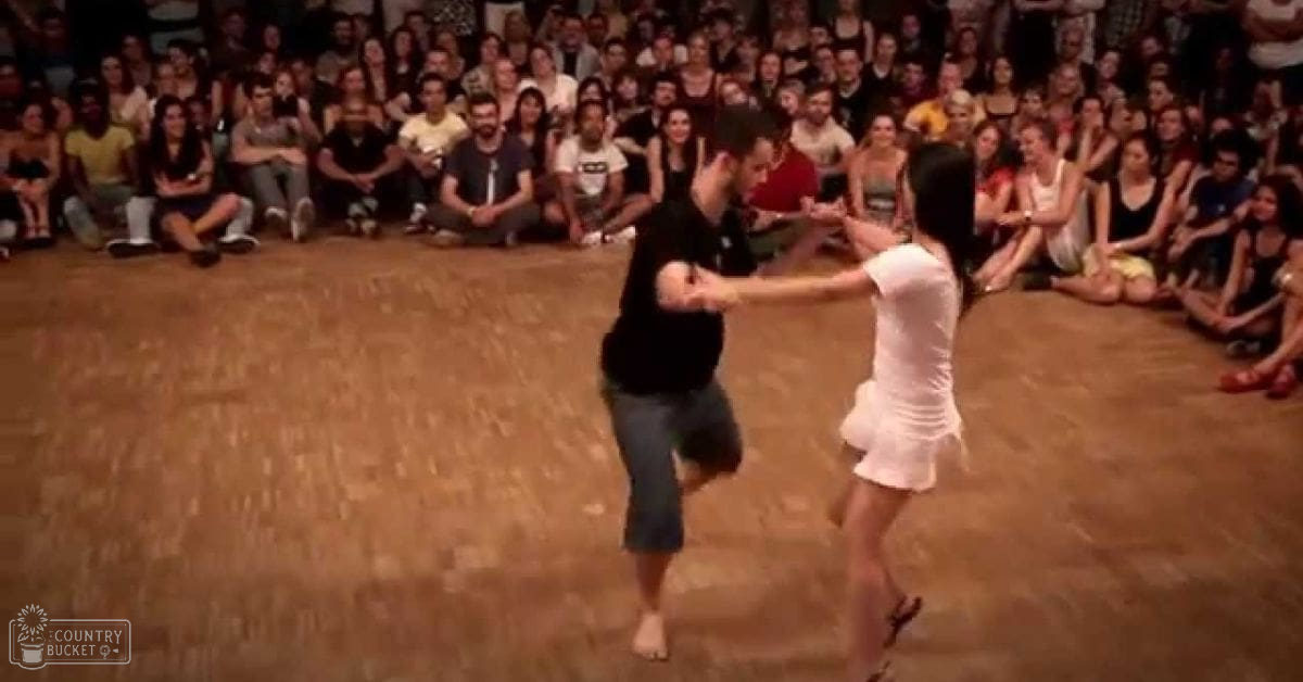 A dance performance by a male and female dancer, young adults to middle-aged audience seated indoors under artificial evening lighting.