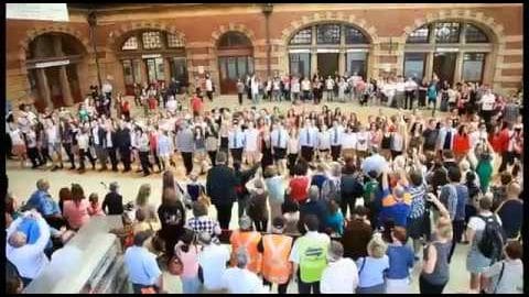 A large crowd gathered in front of an old historical site on a sunny summer day.