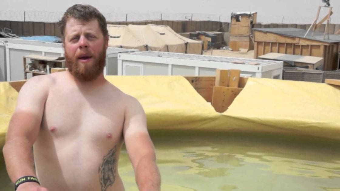 An adult male with tattoos wearing wristband near a pool under yellow tarpaulin, suggesting an outdoor construction or storage area during daytime.