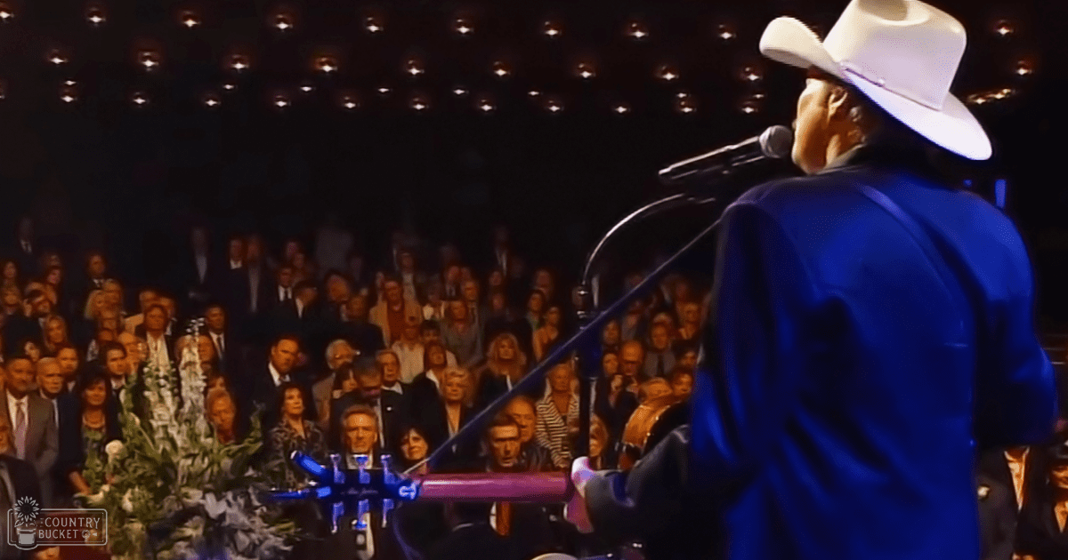A performer in a blue suit and white cowboy hat at an indoor concert, with various attendees in formal attire.