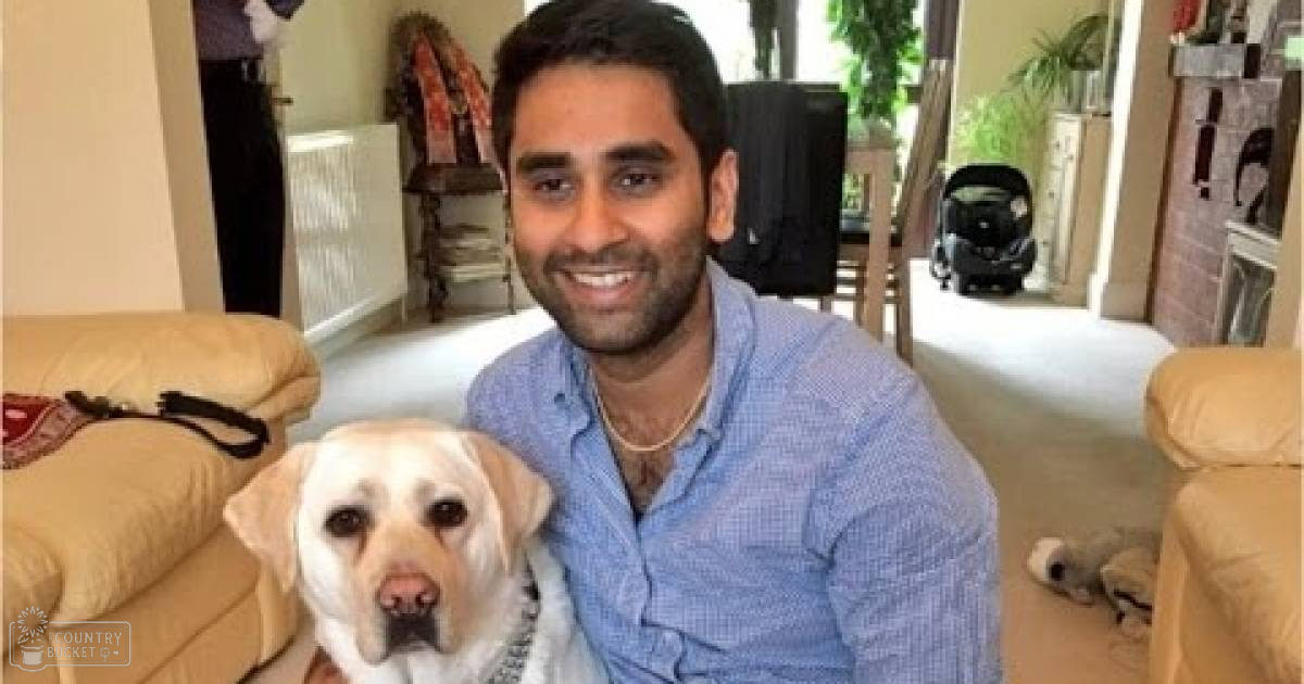 Adult male wearing light blue checkered button-up shirt with beige sofas, yellow Labrador Retriever, family room setting with natural daylight.