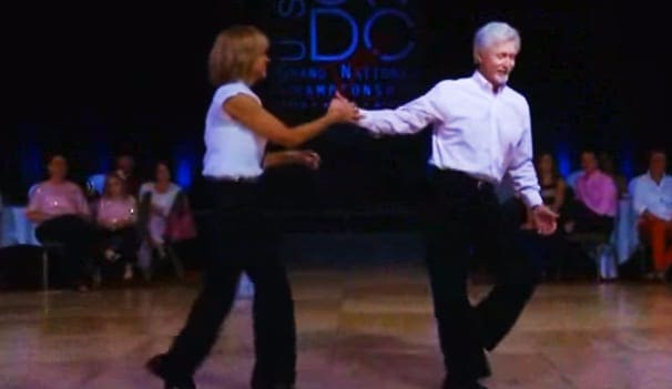 Dance duo performing at USDC Grand National Championships event indoors with formal audience seating.