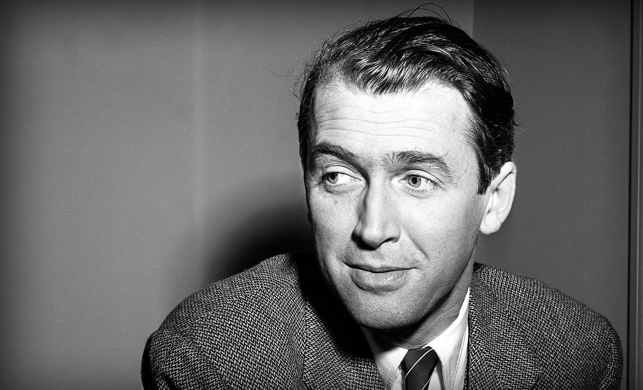 A middle-aged man wearing a textured blazer over a collared shirt with a tie in an indoor setting with even, artificial lighting.