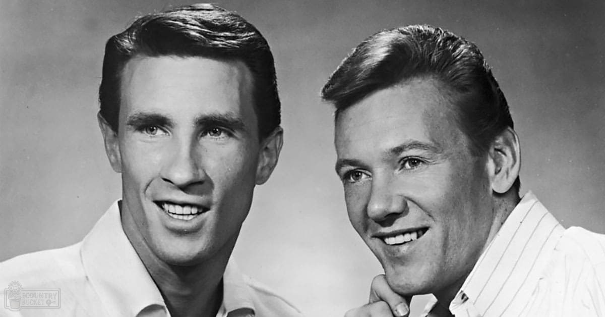 Two young adult males in a neutral studio setting, wearing light-colored striped shirts with subtle patterns, photographed in grayscale.
