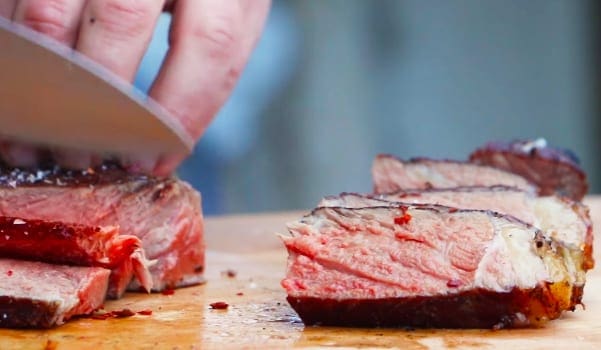A hand cuts a medium-rare steak on a wooden cutting board in an indoor kitchen setting, with blurred background and no visible season or time of day.