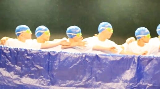 Children playing in a swimming pool with blue tarp at the edge, casual outdoor setting with dark green backdrop