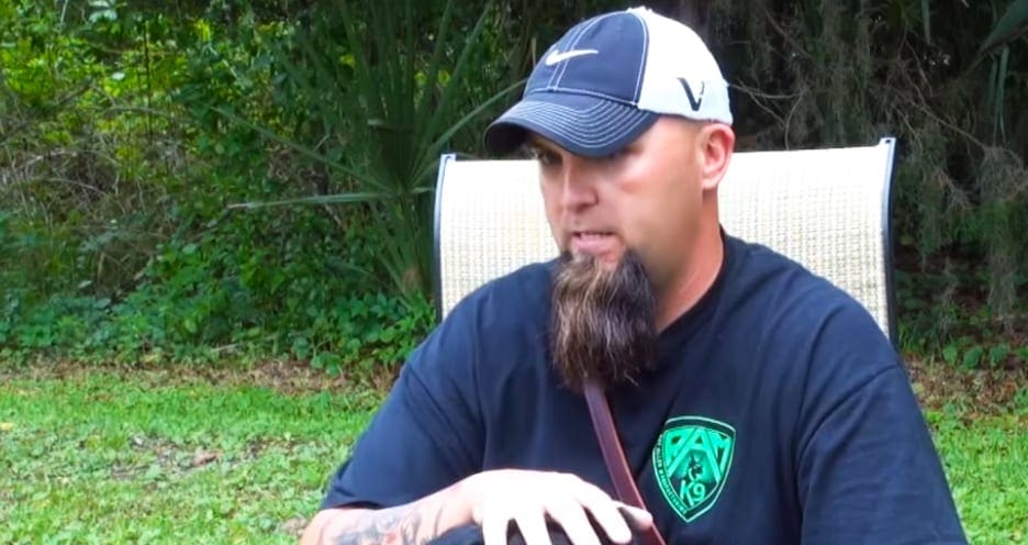 Adult male in a relaxed casual t-shirt with 'RAT 19' logo and white Nike cap, sitting outdoors on green grassy terrain with white woven chair visible behind him.