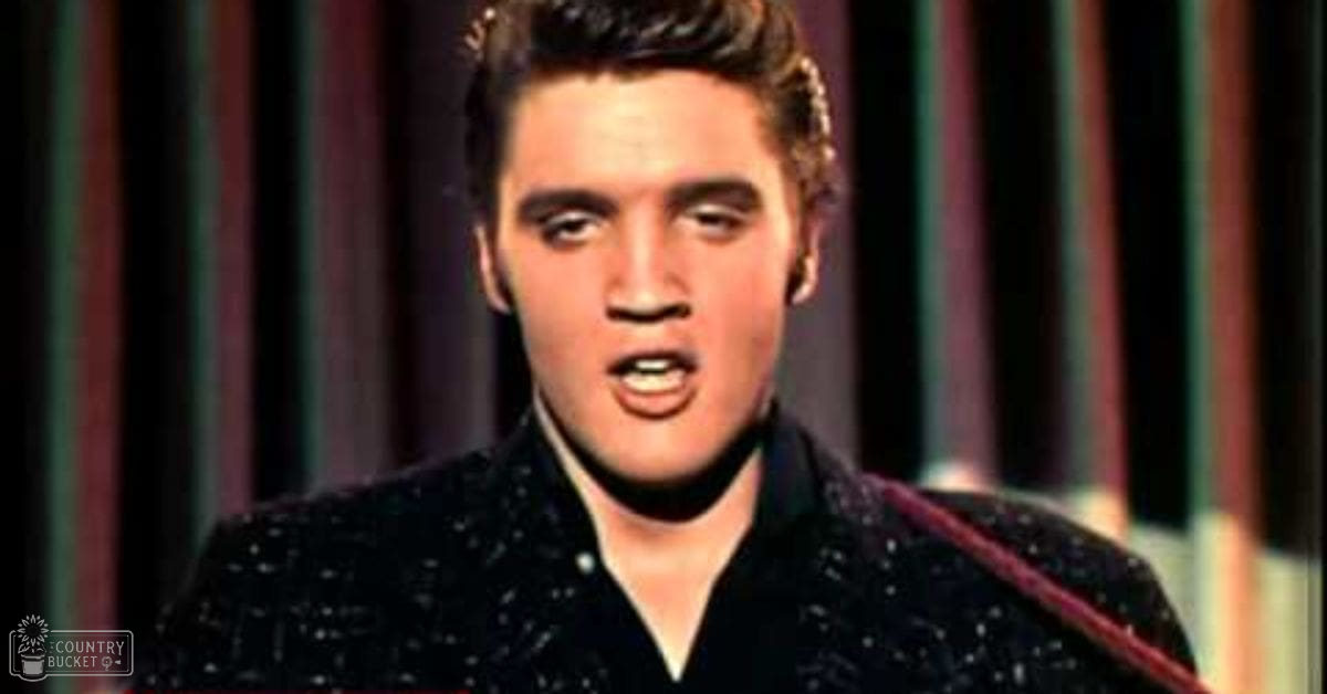 A young adult male wearing a fitted black shirt with small white dot pattern, likely tailored for stage performance, indoors with curtains suggesting a mid-20th century recording or performance studio environment.