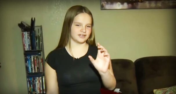 A young adult female wearing a relaxed, black short-sleeved top with a round neckline in an indoor room setting.