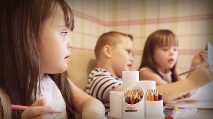 Children engaged in an activity at a table in a classroom setting with light-colored walls with horizontal stripes.