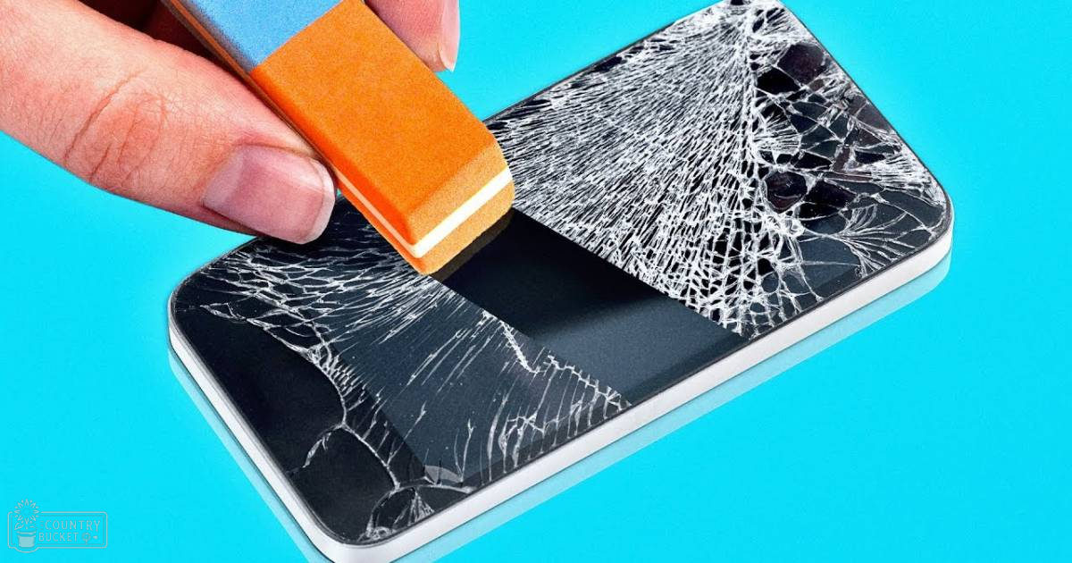 A hand uses an orange eraser to clean a cracked smartphone screen against a solid bright blue background.