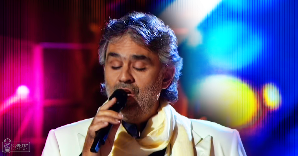 A middle-aged adult male performing on stage under vibrant blue and pink lighting at an indoor concert venue.