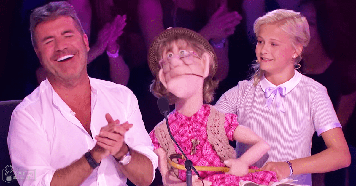 A young female performer wearing a vintage-style pink plaid dress with ruffled sleeves, standing before judges at an indoor talent show.