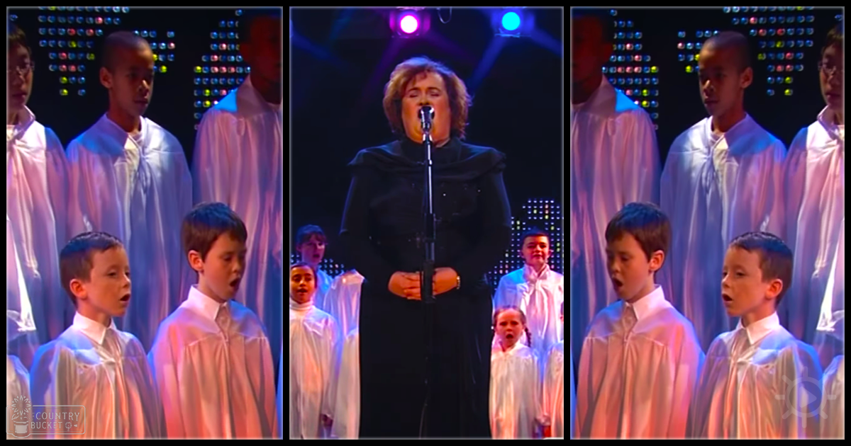 A woman singing in front of a choir on an indoor stage under colorful lights.
