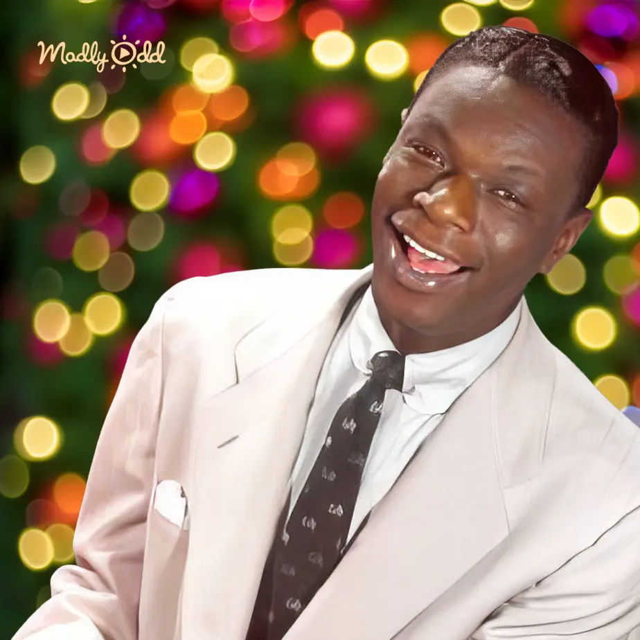A young adult male in a well-fitted light-colored suit jacket, white dress shirt, and patterned tie stands indoors with festive lighting.
