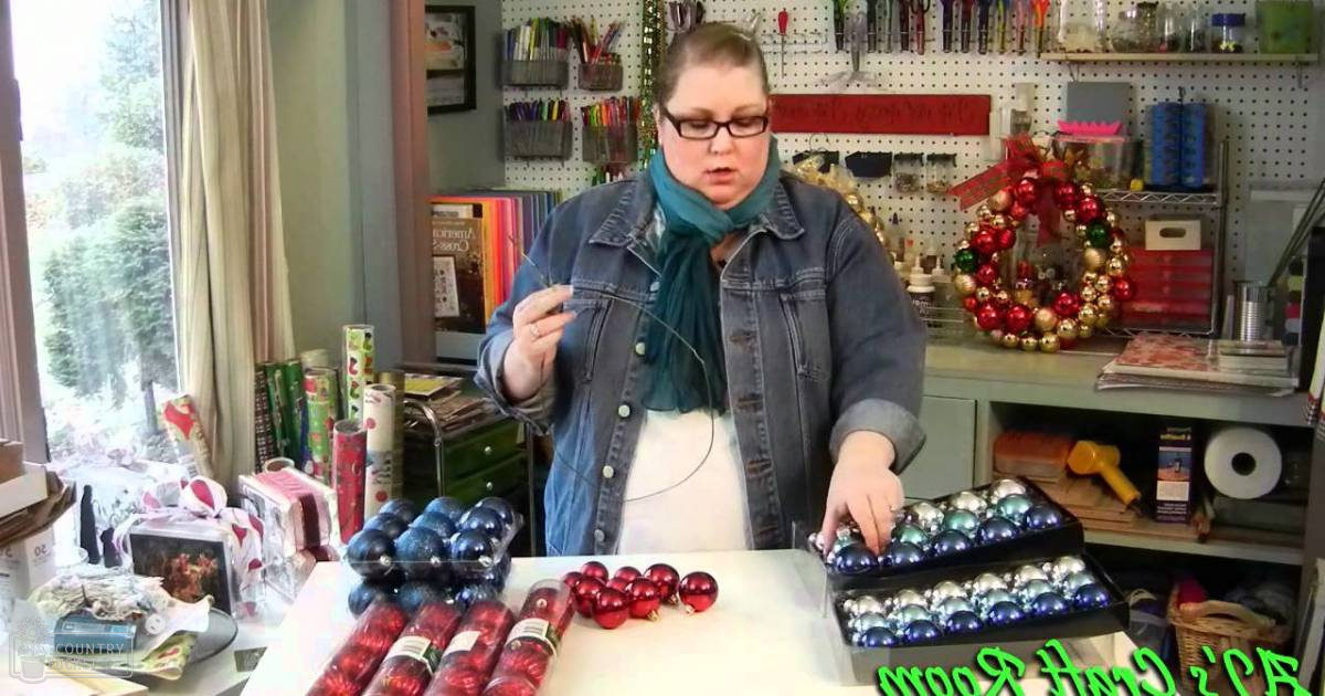 A middle-aged woman wearing a denim jacket over a white top with a teal scarf is shopping in an indoor craft or gift shop filled with Christmas ornaments and crafting supplies.