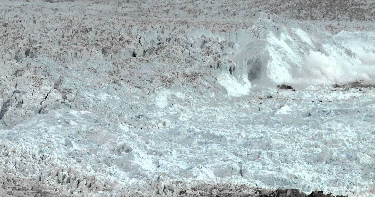 A vast expanse of ice and snow under a natural daylight, set against the backdrop of a mountainous region with glaciers.