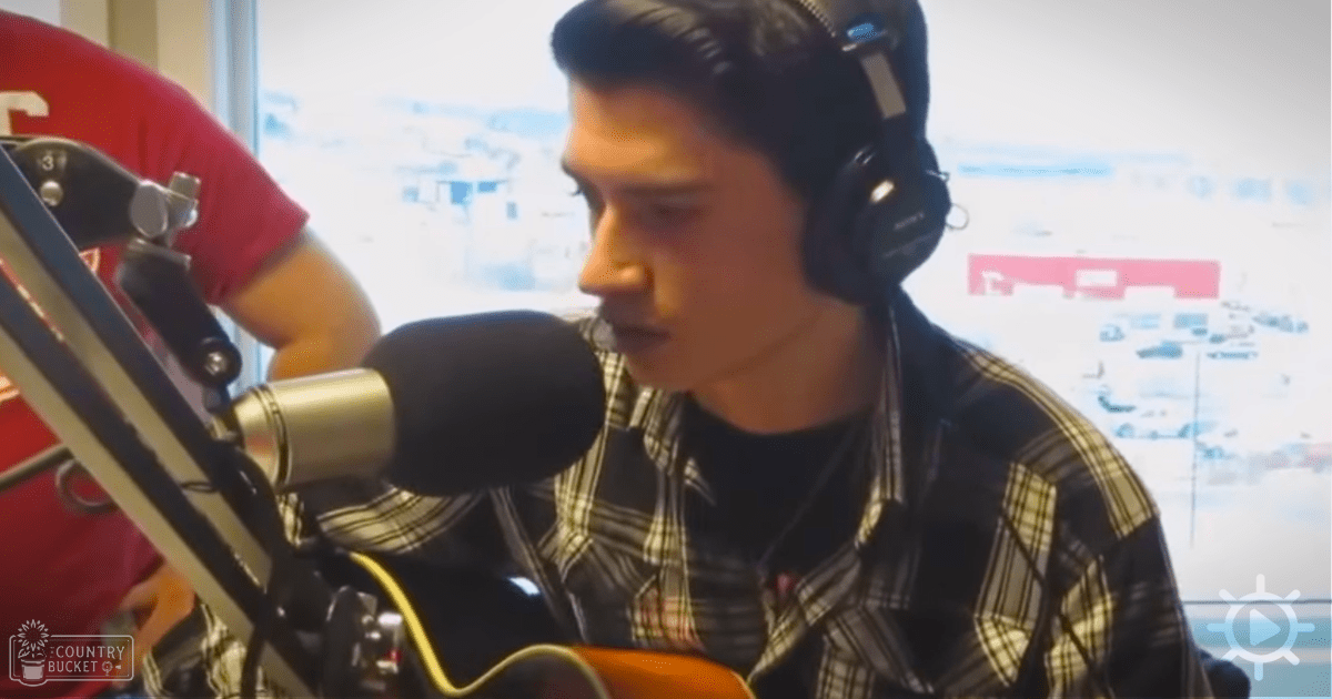 A young adult male in a recording studio, wearing a plaid shirt with black and white stripes and headphones around the neck.