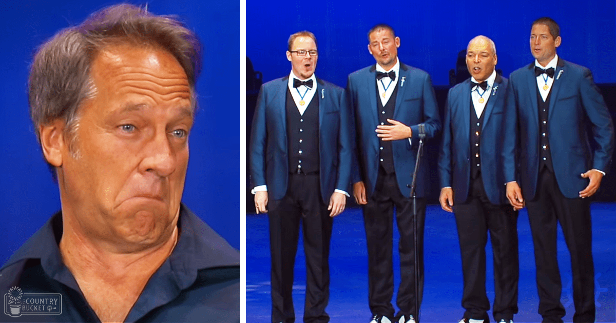 A middle-aged man with short gray hair and blue eyes wearing a dark blue open-collared shirt, reacting to something indoors, possibly in a television studio or stage performance area.