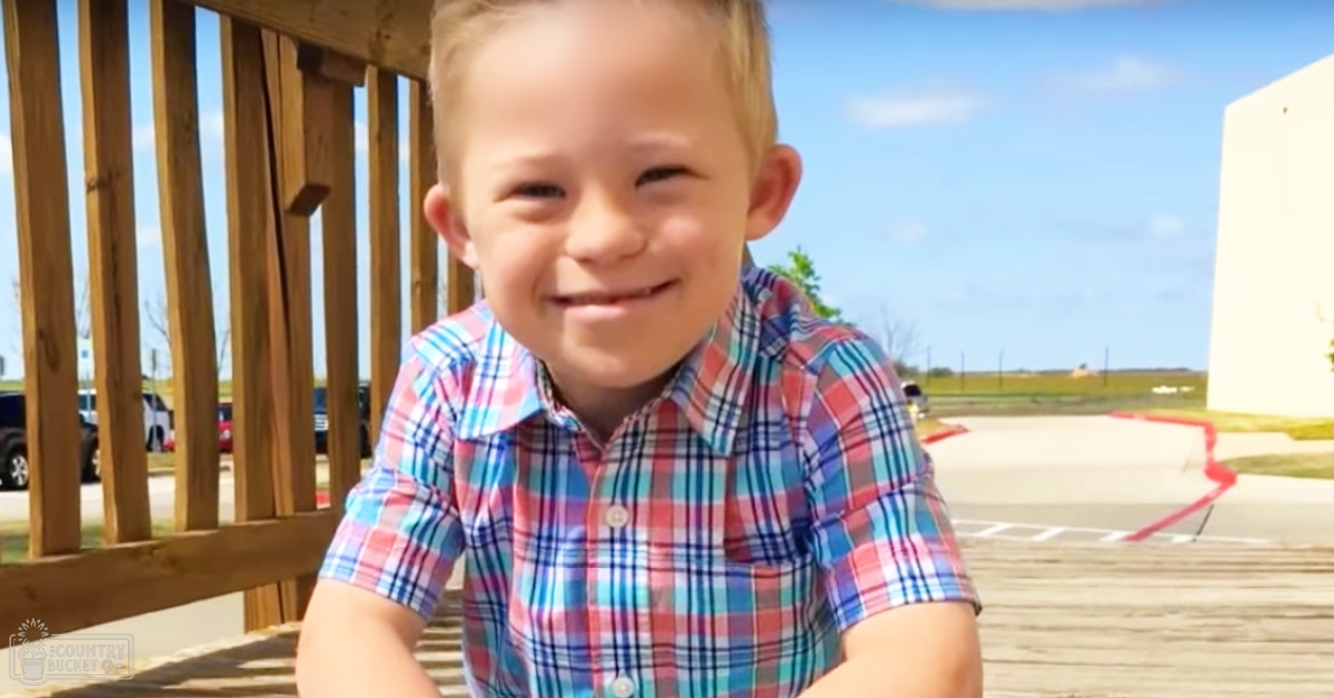 A toddler wearing a red, white, and blue plaid button-down shirt in an outdoor setting with wooden structures and parked cars.