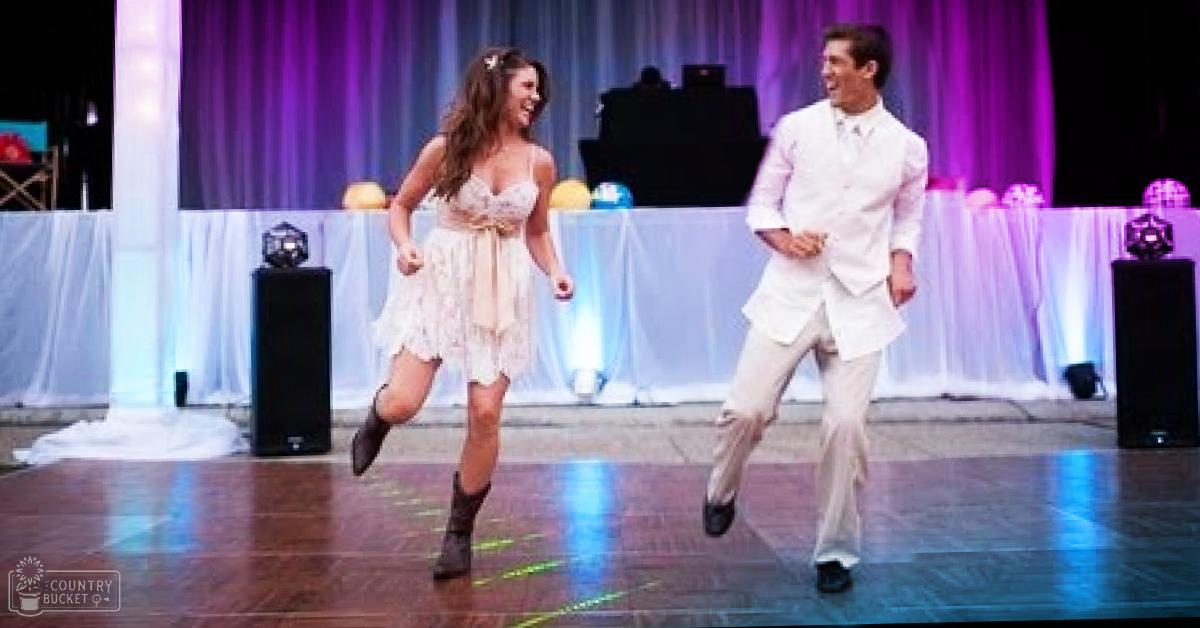 Young adults dancing in a festive indoor event space with stage lighting and decorative elements.