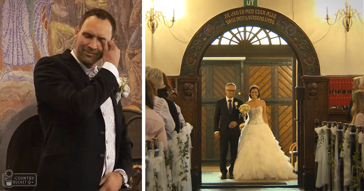 Adult male groom wearing a black suit and boutonniere, standing with an adult female bride in a white wedding gown at an ornate church setting during a wedding ceremony.