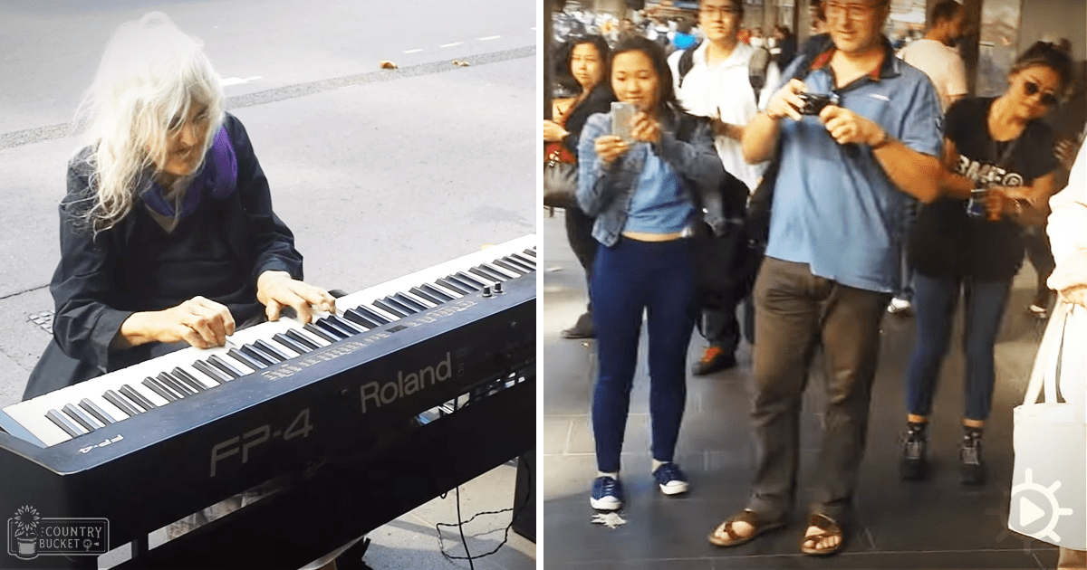 An older adult female street performer playing an electronic keyboard in a public space with other people taking photos and videos around her.