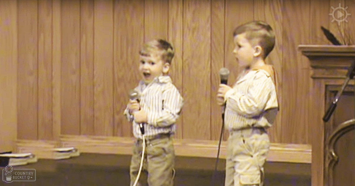 Two young boys in striped button-up shirts performing in a room with wood paneling, wearing wristwatches.