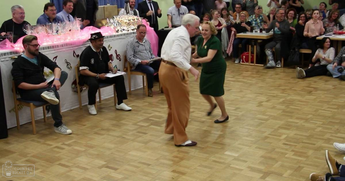 A community hall scene with people dancing and seated, with trophies on a table in the background.