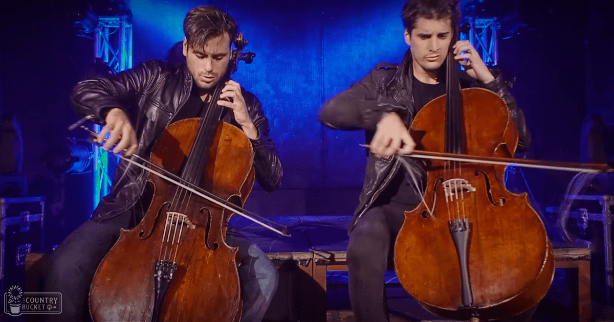 Two young adult male musicians in black leather jackets performing on stage with blue lighting and musical equipment visible.