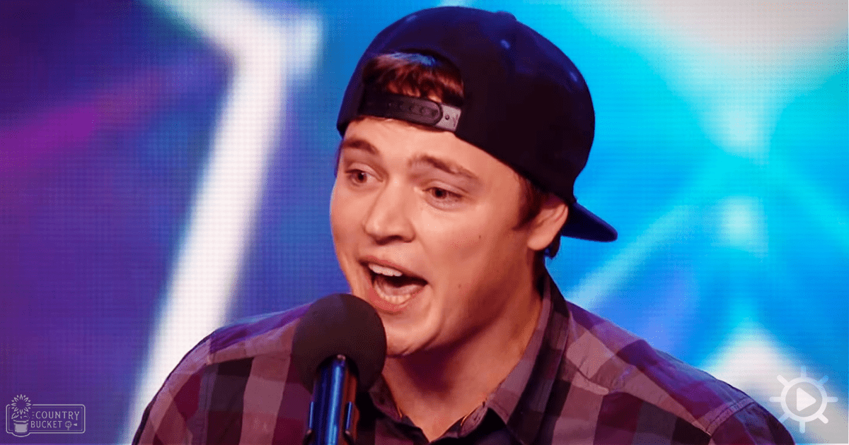 A young adult male wearing a black baseball cap, a plaid shirt, sings into a microphone on stage with vibrant blue and purple lighting in what appears to be a talent show setting.
