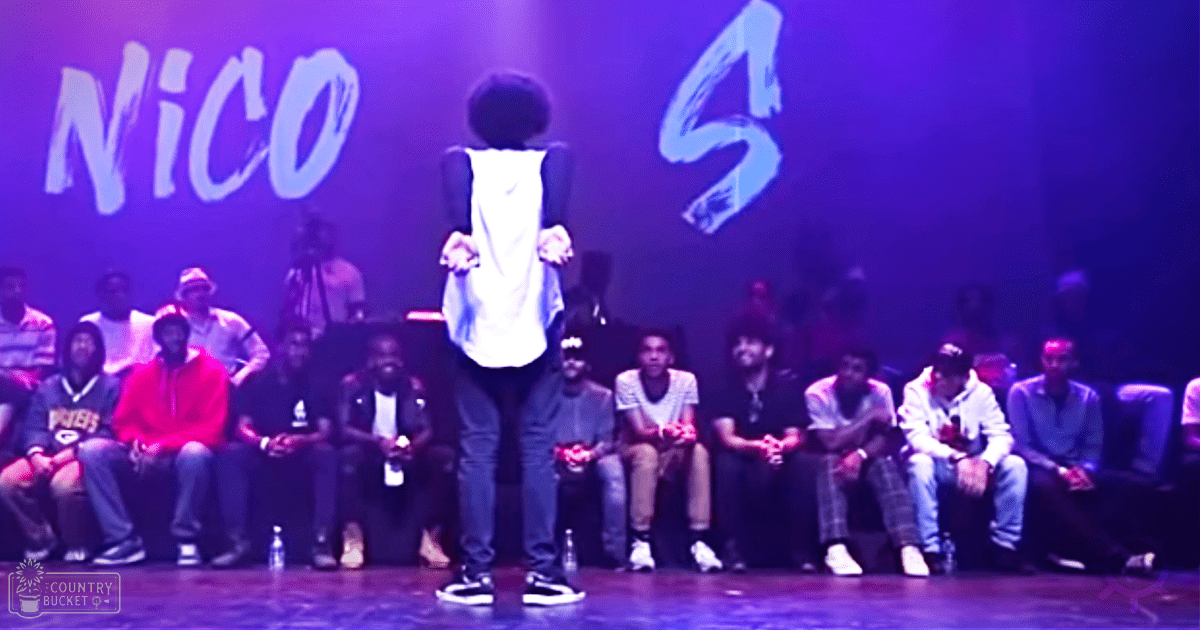 A performance scene with an adult female performer and a diverse audience of teenagers in casual attire, under artificial stage lighting at night.