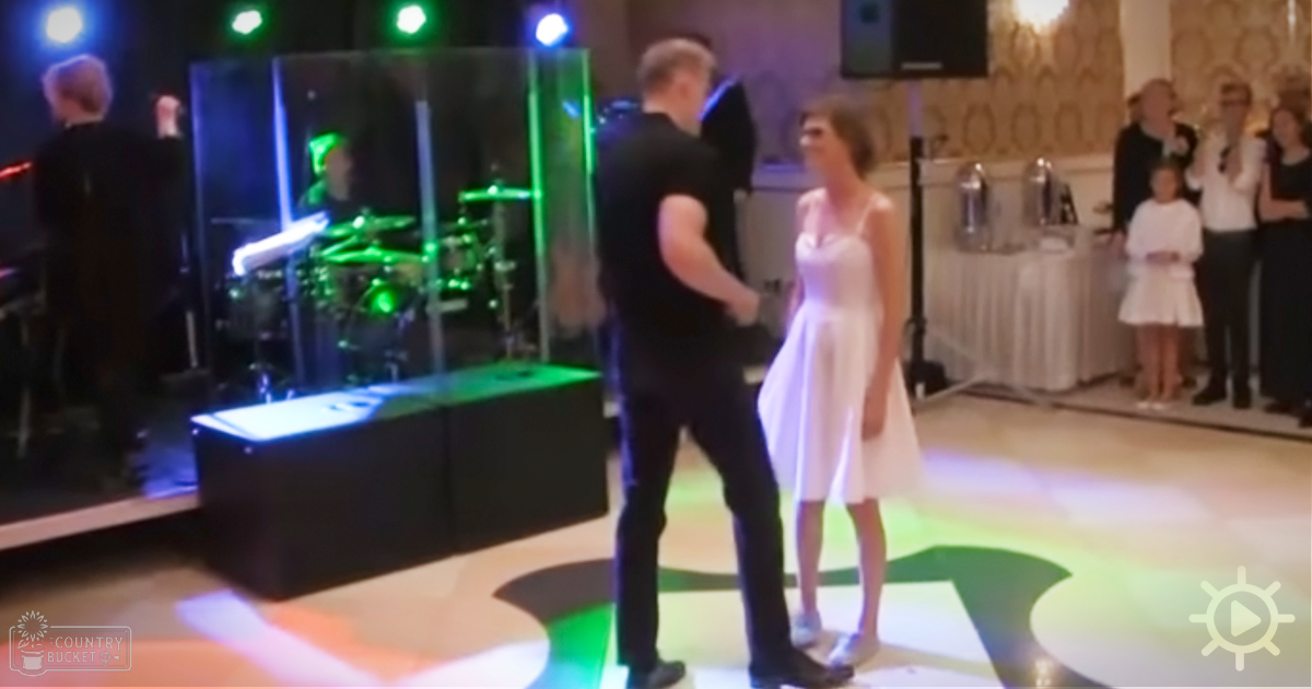 A couple dancing at an indoor event with a DJ booth and drum set visible in the background.