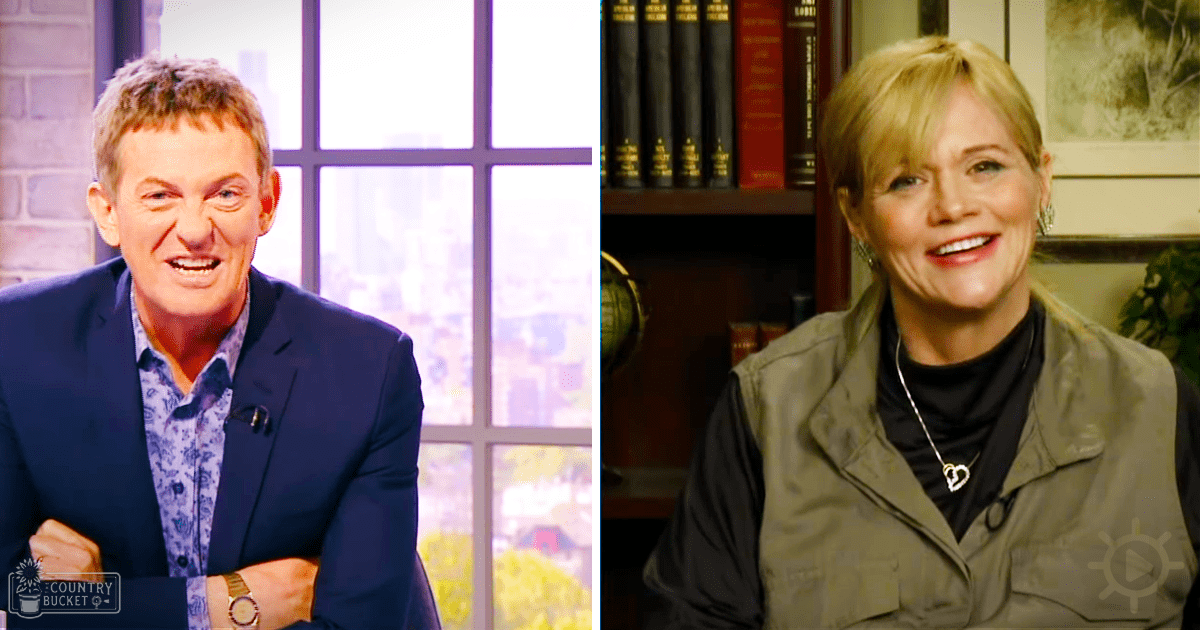 Two individuals posed indoors, one wearing a dark blue blazer over a patterned shirt, and another in an olive green jacket with black turtleneck sweater; urban landscape visible through the window suggests daytime setting.