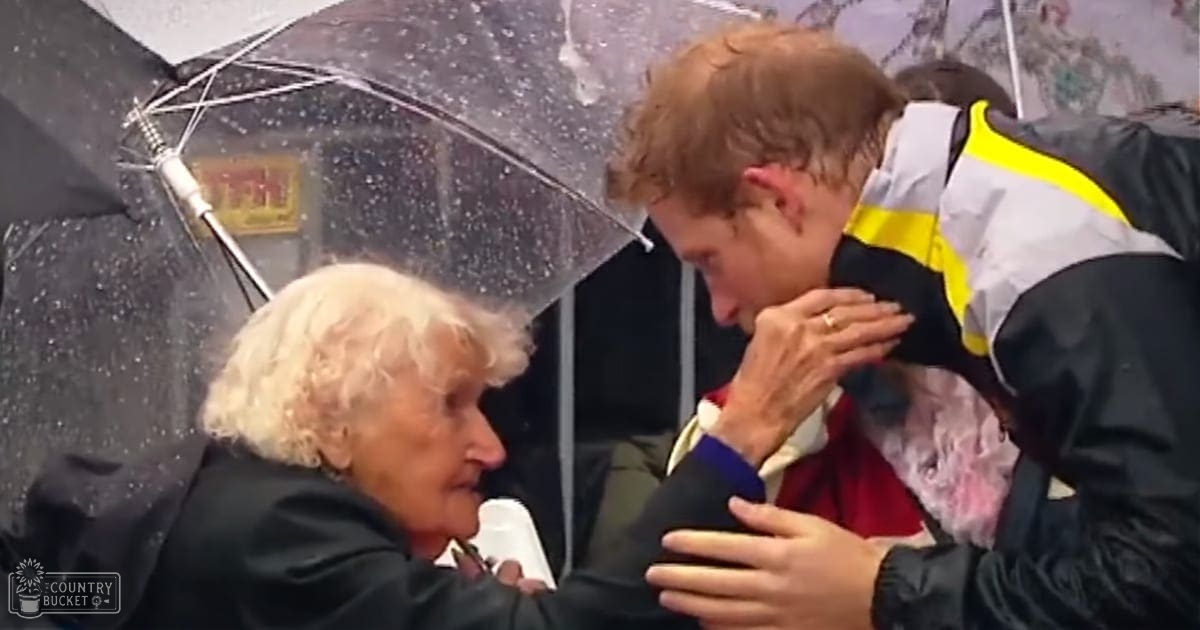A young adult male interacts gently with an older middle-aged woman in a public setting, holding a transparent umbrella under rain, suggesting a comforting gesture.