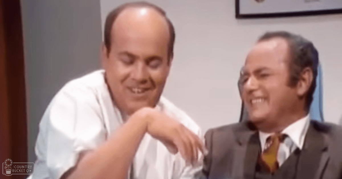 Two middle-aged men in formal attire indoors; one wears a white shirt with a relaxed fit, and the other dons a dark suit jacket, white dress shirt, and patterned tie.