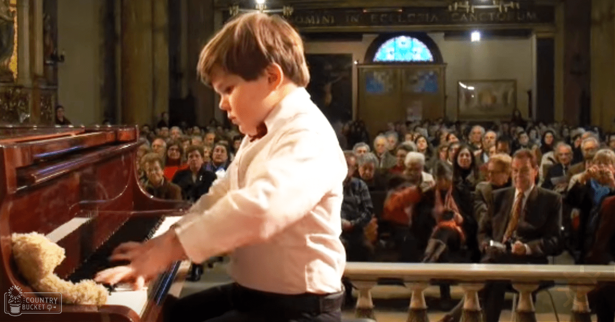 A toddler playing piano in a church setting surrounded by seated adults, with stained glass and ornate architecture visible.