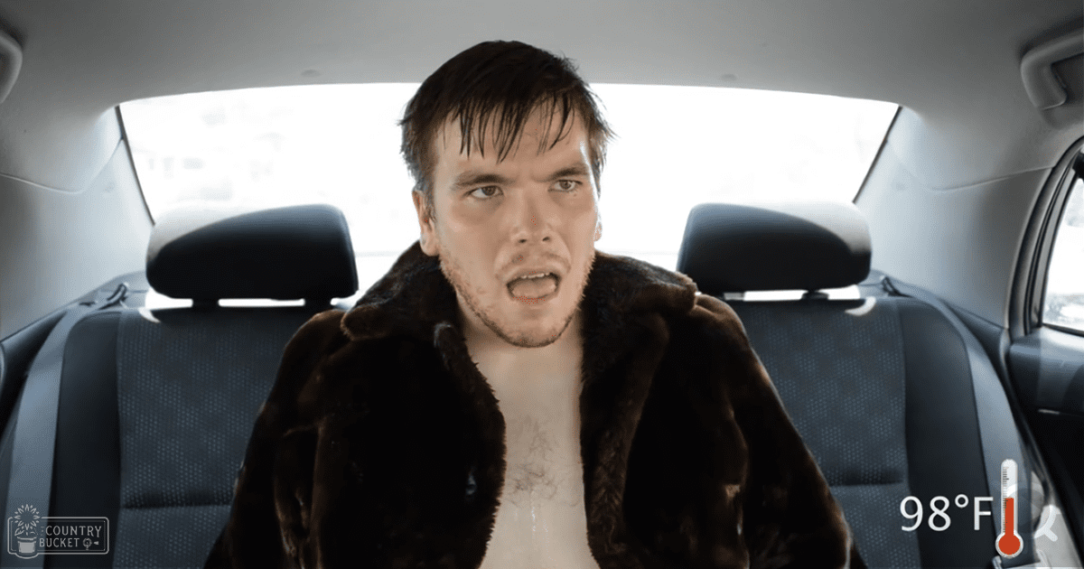 A young adult male wearing a brown fur coat sits in the back seat of a modern car on an overcast day with a thermometer graphic indicating 98°F (37°C).