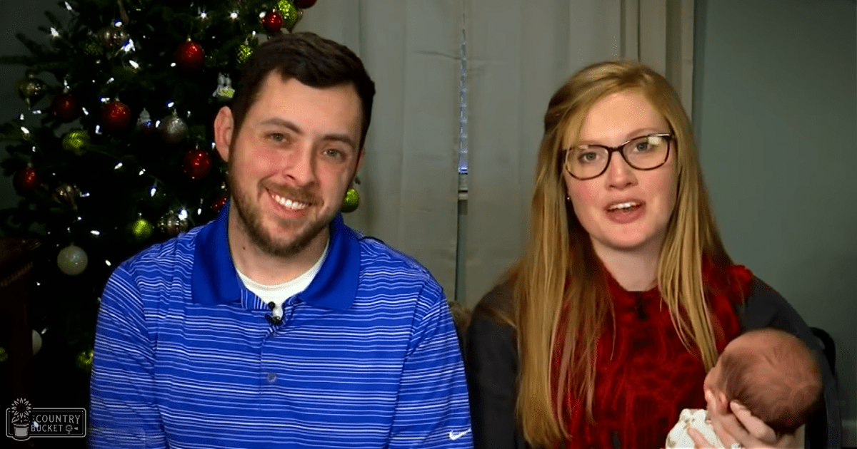 A young adult male in a blue and white striped polo shirt stands beside an adult female wearing a red top and dark jacket, both indoors near a decorated Christmas tree during the holiday season.