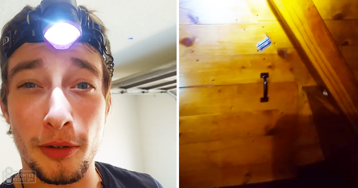 A young adult male in a relaxed, dark-blue t-shirt stands amidst wooden walls and ceiling beams, possibly an attic or loft space with artificial lighting suggesting evening.