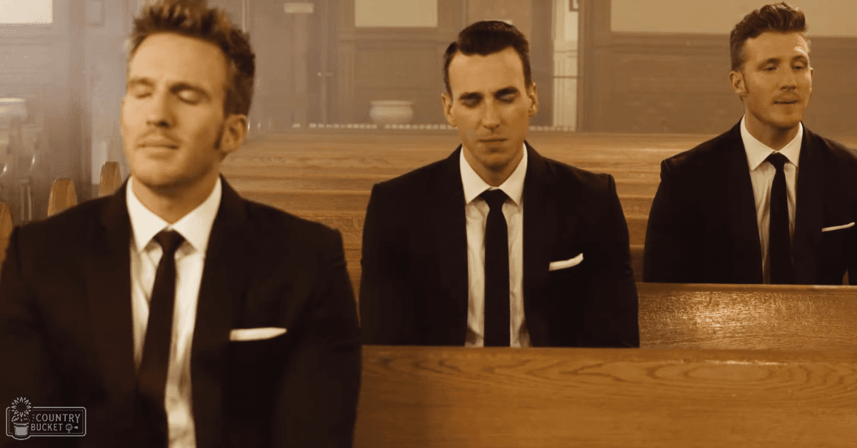 Three young adult men in formal attire seated on wooden pews inside a church, likely during daytime or early evening with natural light.