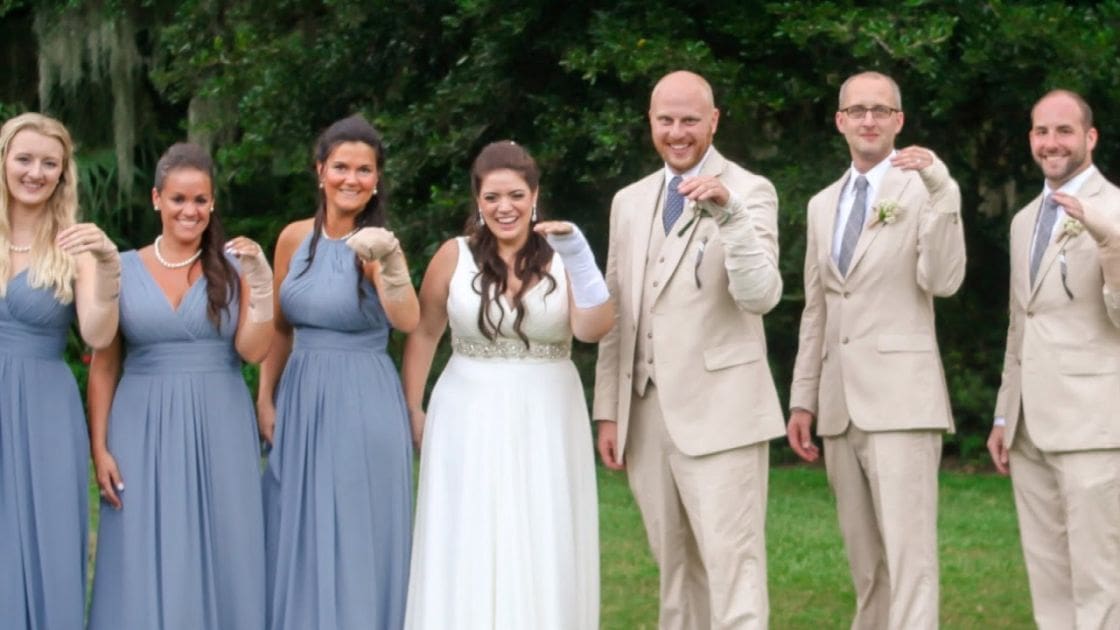 A wedding party in an outdoor setting with greenery, soft daylight, and blue skies.