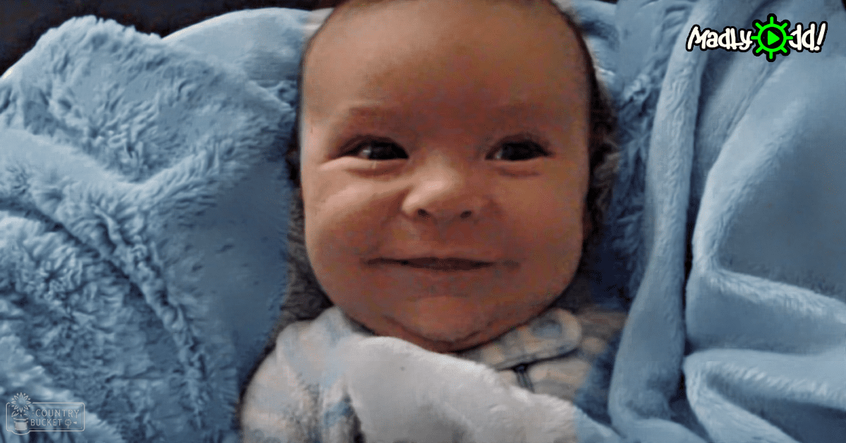 An infant wearing a light blue garment with small white dots, lying on a bed covered with matching light blue blankets in an indoor setting.