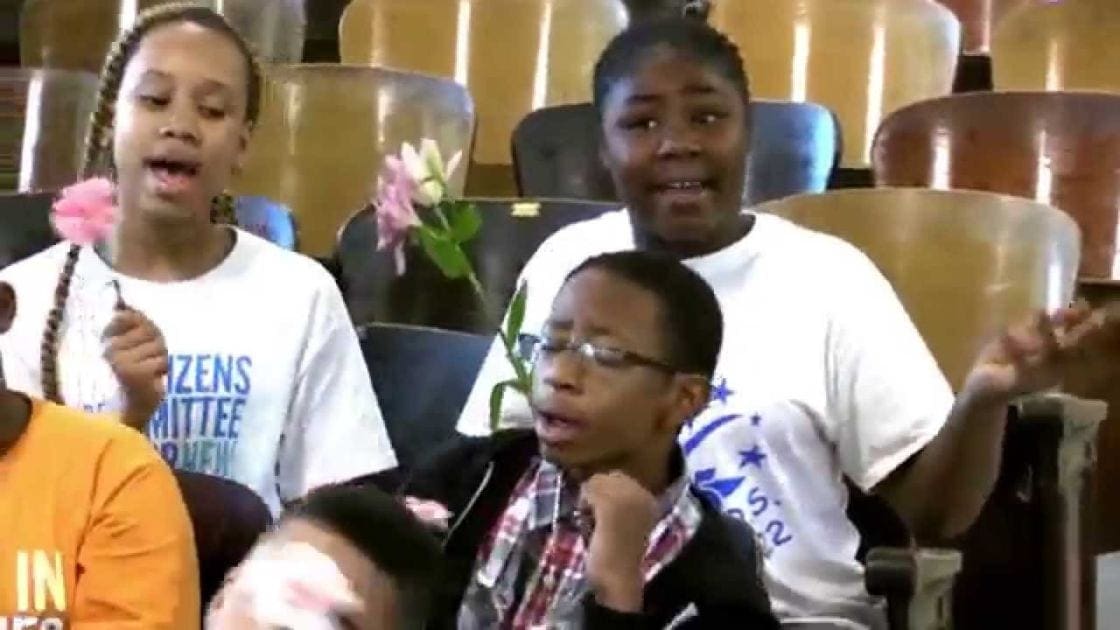 Three children in white t-shirts with blue stars, standing indoors in a community center or school setting.