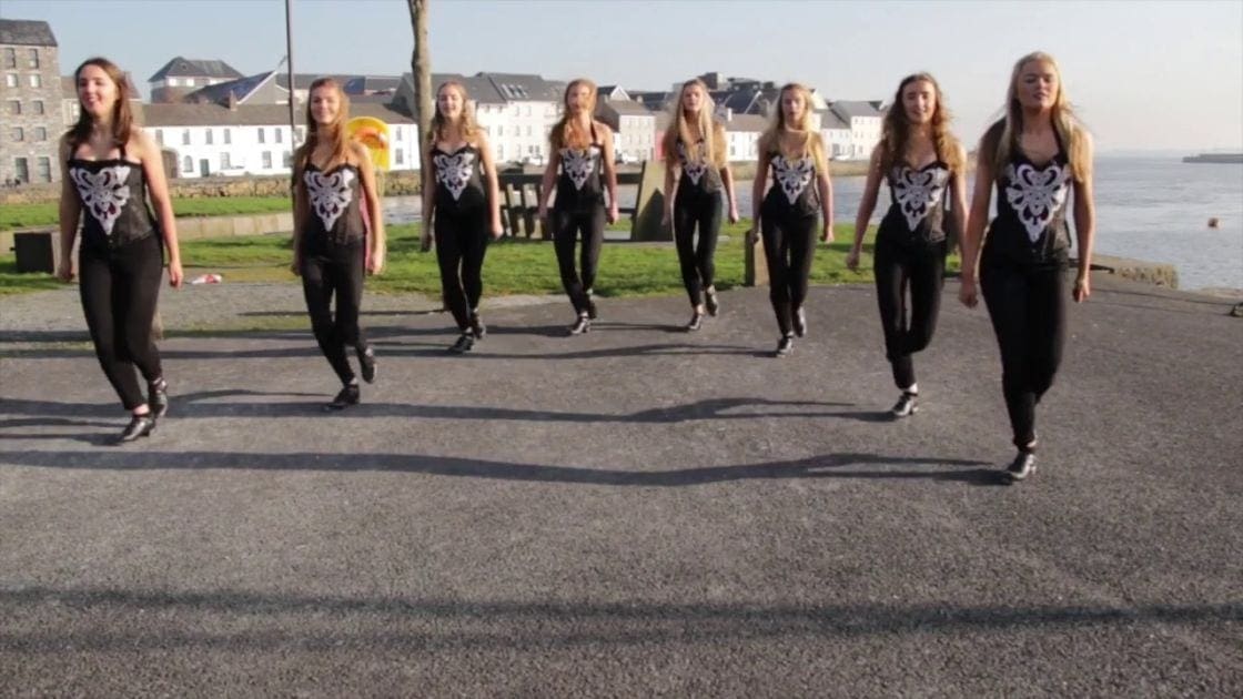 Young adult females performing on an outdoor promenade near water, clear skies, late afternoon light.