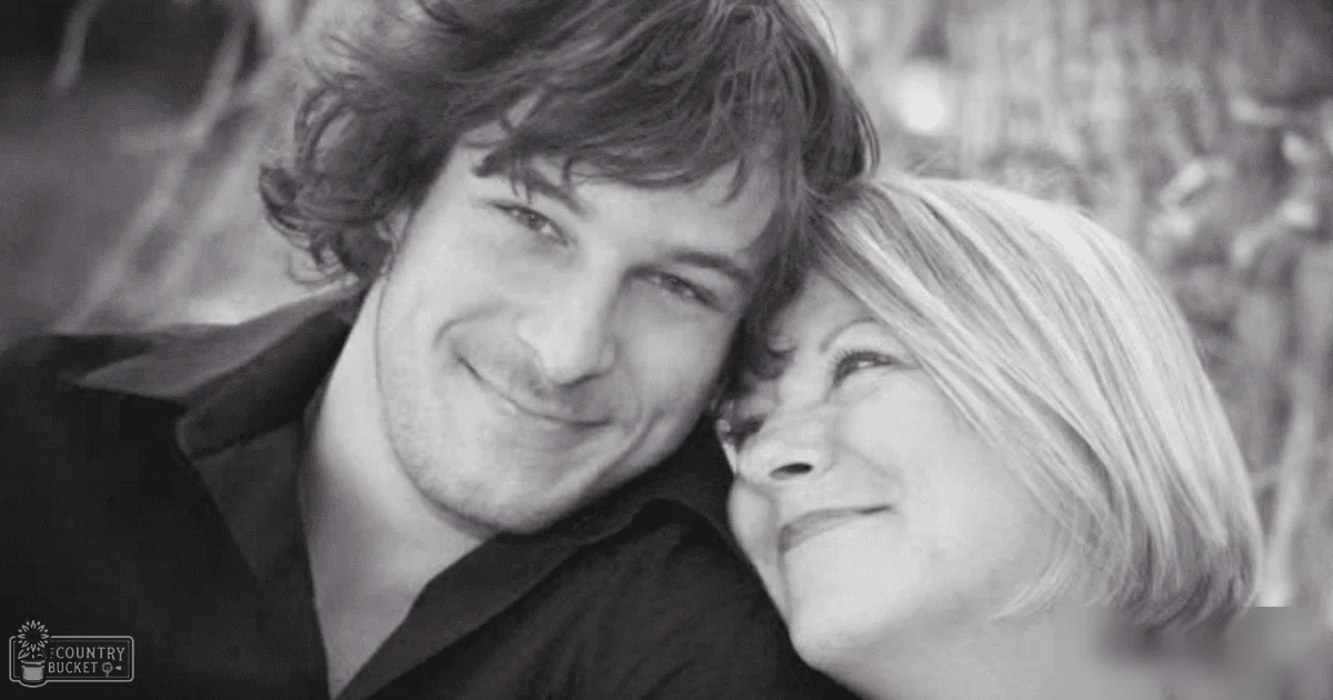 Young adult male wearing a dark, long-sleeved shirt in an outdoor wooded setting; older adult female dressed in light-colored clothing with natural lighting and grayscale tones.
