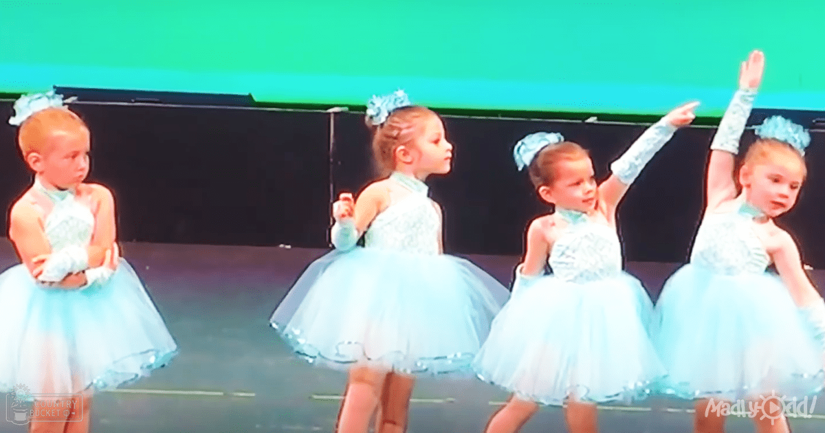 A group of young female children in light blue tutu dresses performing on stage with a green background and 'Madly Odd!' text visible.