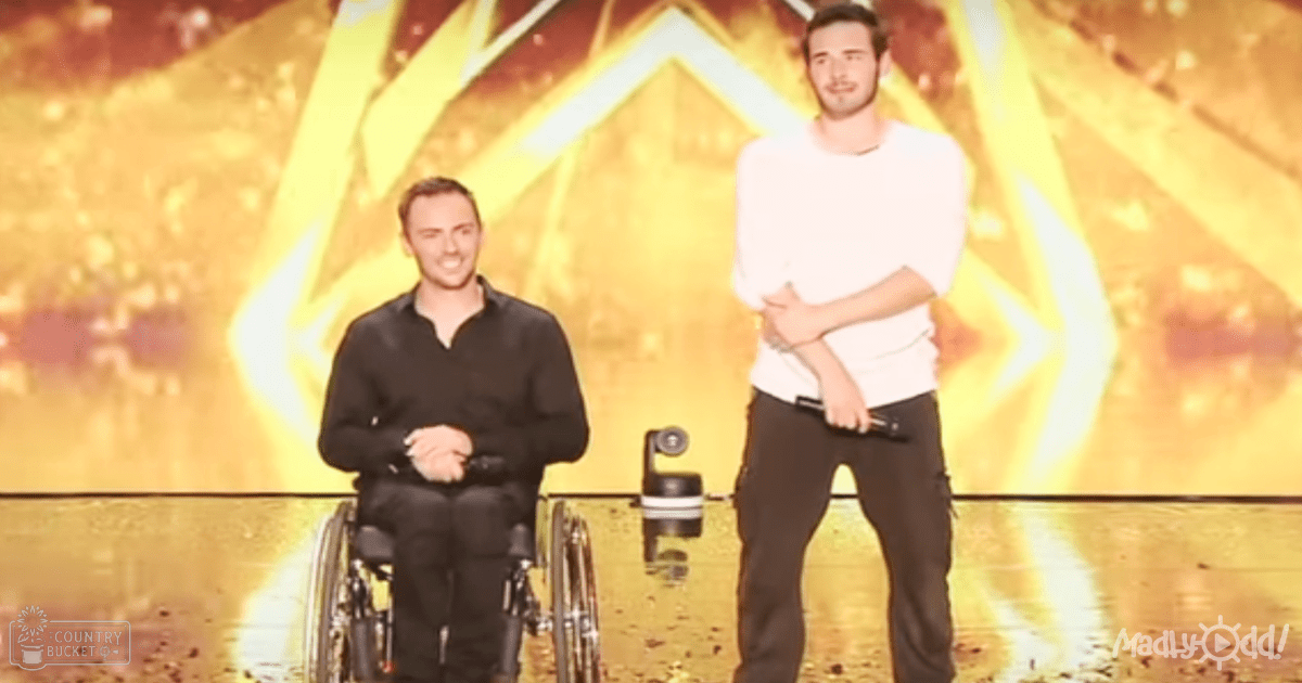 Two young adult males in formal attire are seated and standing on stage, with dynamic abstract designs behind them. The setting appears to be an indoor venue during the evening.